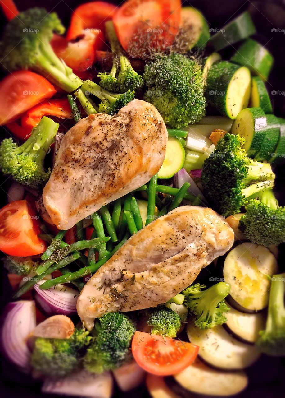 Two roasted chicken breasts on the tray with vegetables
