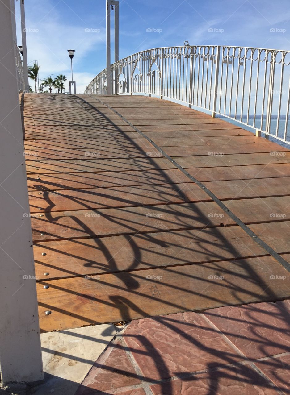 Iron foot bridge over an inlet to the bay with dolphin motif shown in shadows