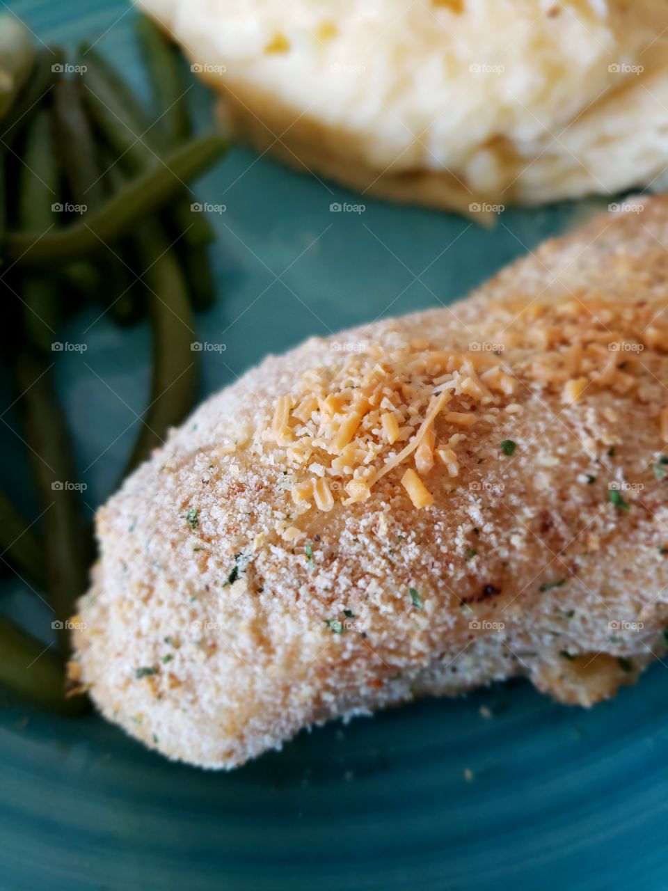 Fine details on a freshly baked chicken breast on a plate served with mashed potatoes and green beans.