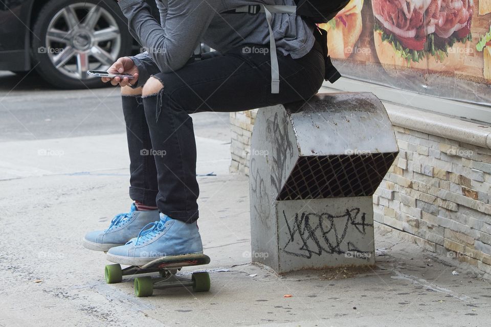 A skateboarder seated on a make shift bench as he checks his smartphone