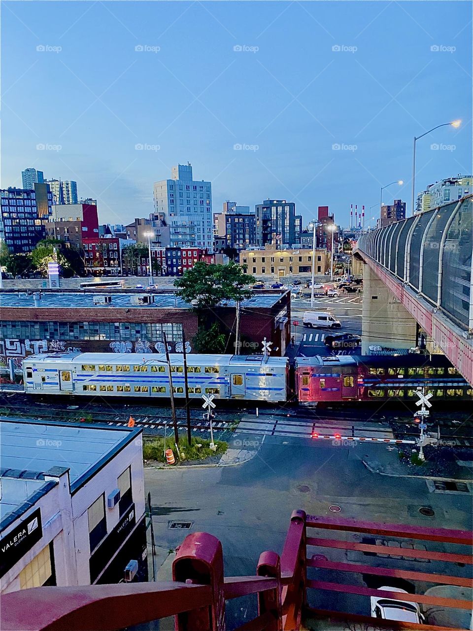 The “Long Island Railroad” is passing us by going underneath the “Pulaski Bridge”. The photo was taken from the top of the staircase of the bridge on the LIC, Queens side. 2023. Hypnotic Productions