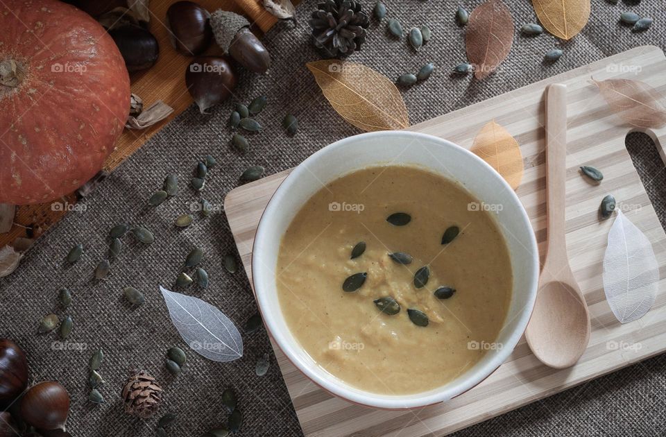 A bowl of cream of pumpkin soup, viewed from above against a background of autumnal ingredients 