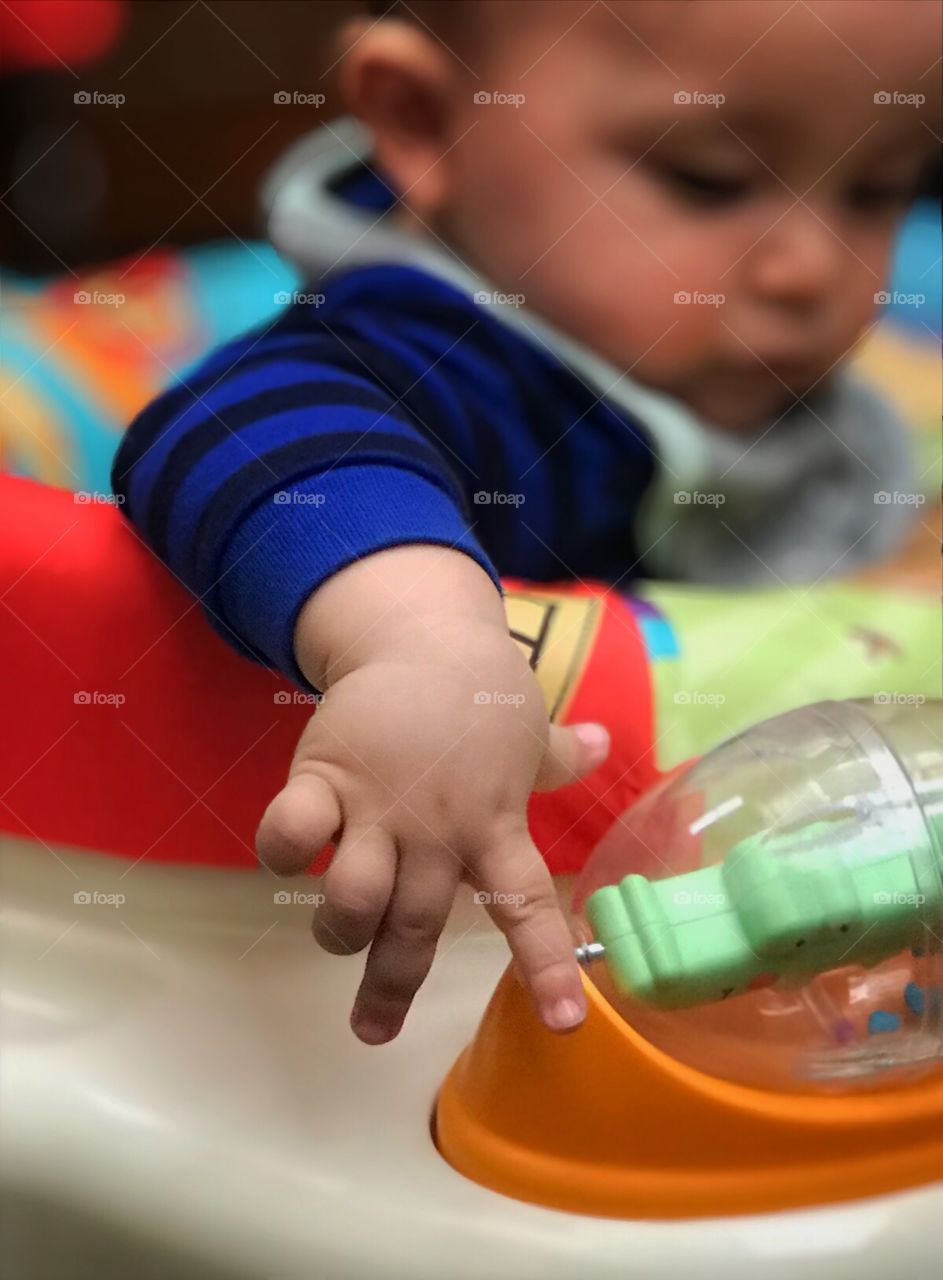 Close up of a baby’s hand as he plays with a toy in his seat.