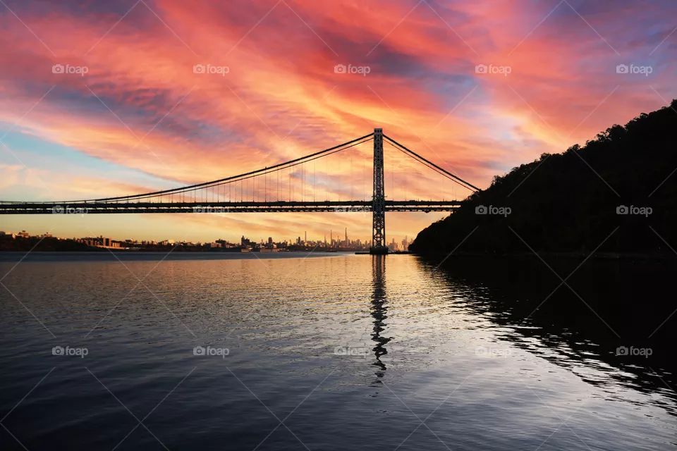 Along the Hudson River underneath the famous George Washington Bridge seen from the vantage point of Fort Lee Historic Park an amazing sunset lights up the distant sky.