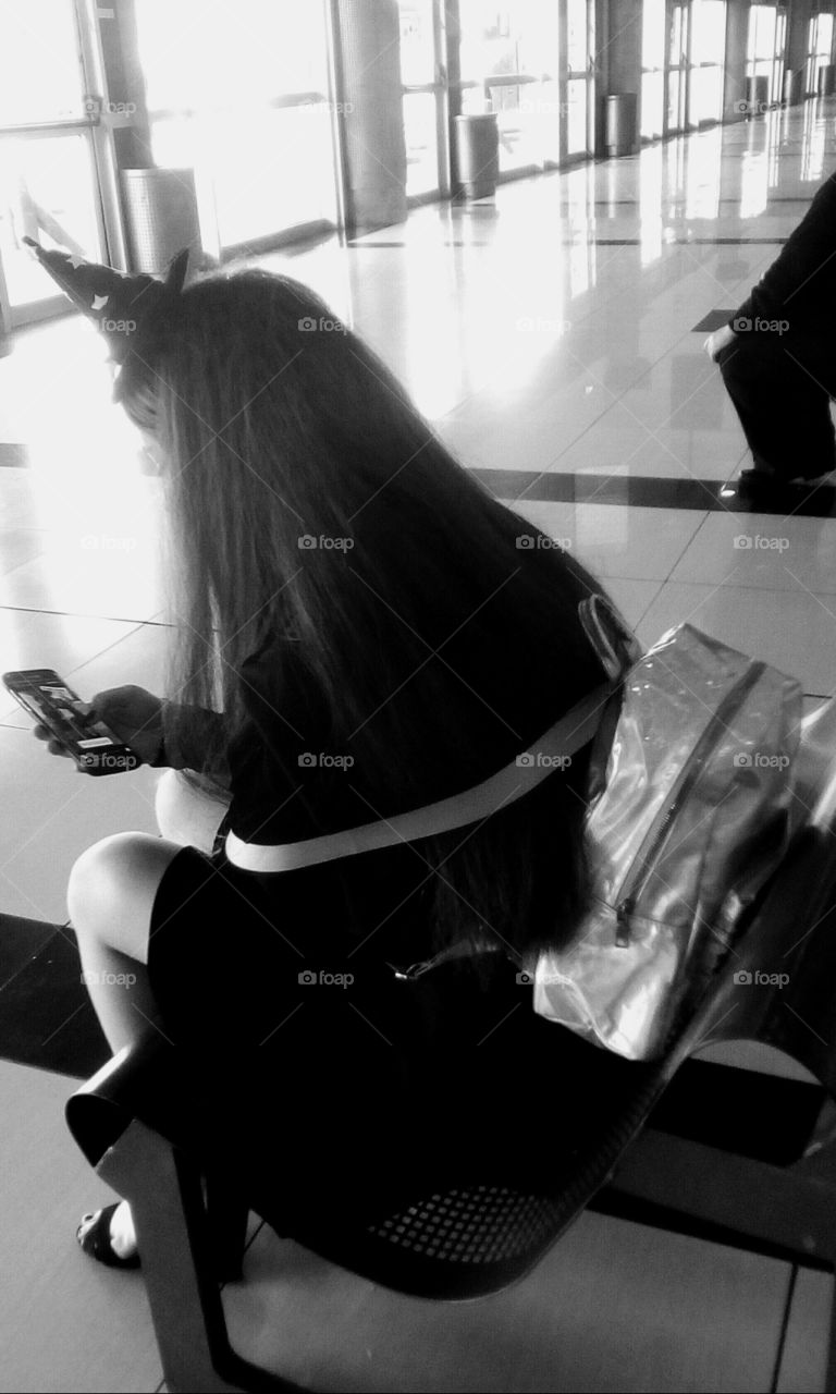 Beautiful young women with long hair
sitting on bench and looking to her 
phone in bus station