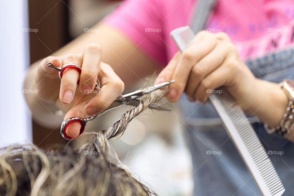 Hairdresser cutting the hair, beauty care concept. Closeup on hands with scissors.