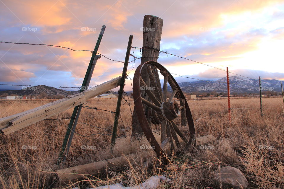 wagon wheel on fence post in field at sunset