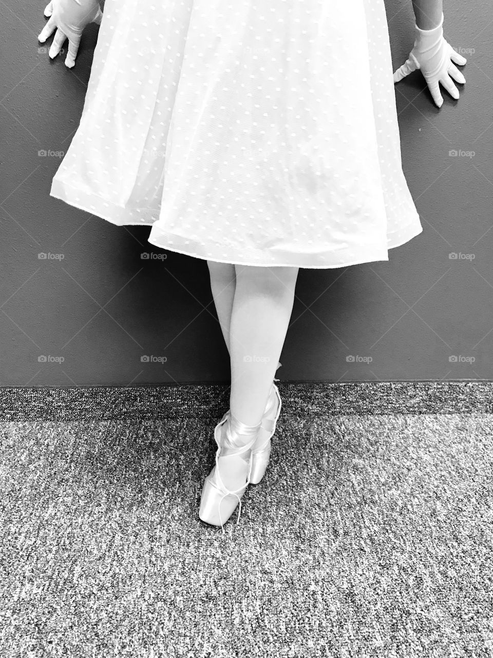 Beautiful ballerina in her toe ballet shoes leaning against a wall with precious skirt and white gloves. 
