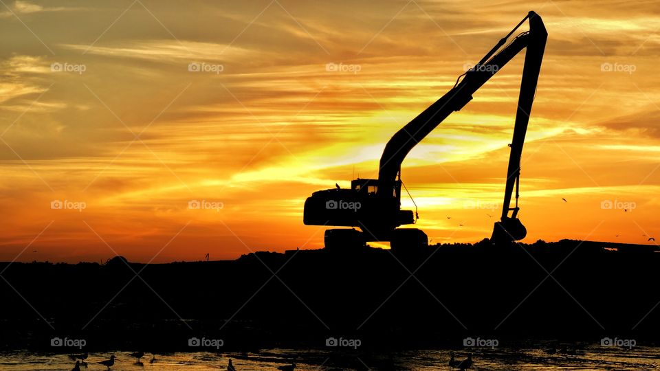 Backlit long reach excavators at sunset