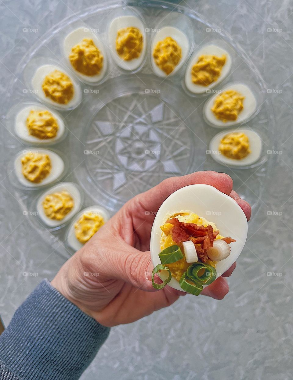 Woman eating deviled eggs, deviled eggs on an egg plate, woman holding deviled egg in her hands, looking down at the appetizer, eating the delicious recipe, appetizer for dinner party, favorite foods 