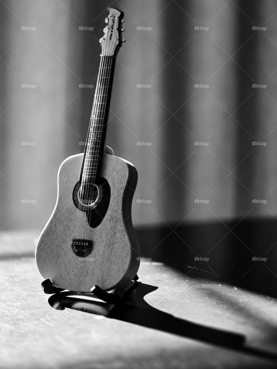 Small collection guitar placed on a table while receiving sunlight on it, in monochrome style.