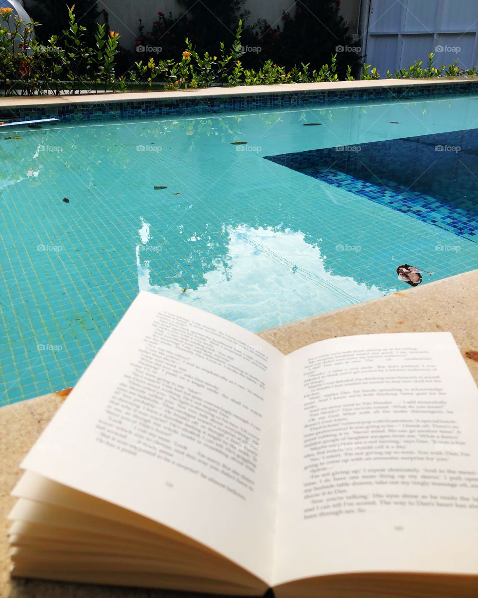 An open book by the pool on a sunny  hot summer day
