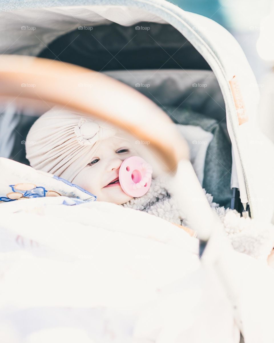 Happy baby falling asleep while smiling in a stroller with a pacifier in her mouth