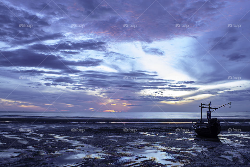 The morning sun light in the sea and the boat on the beach.