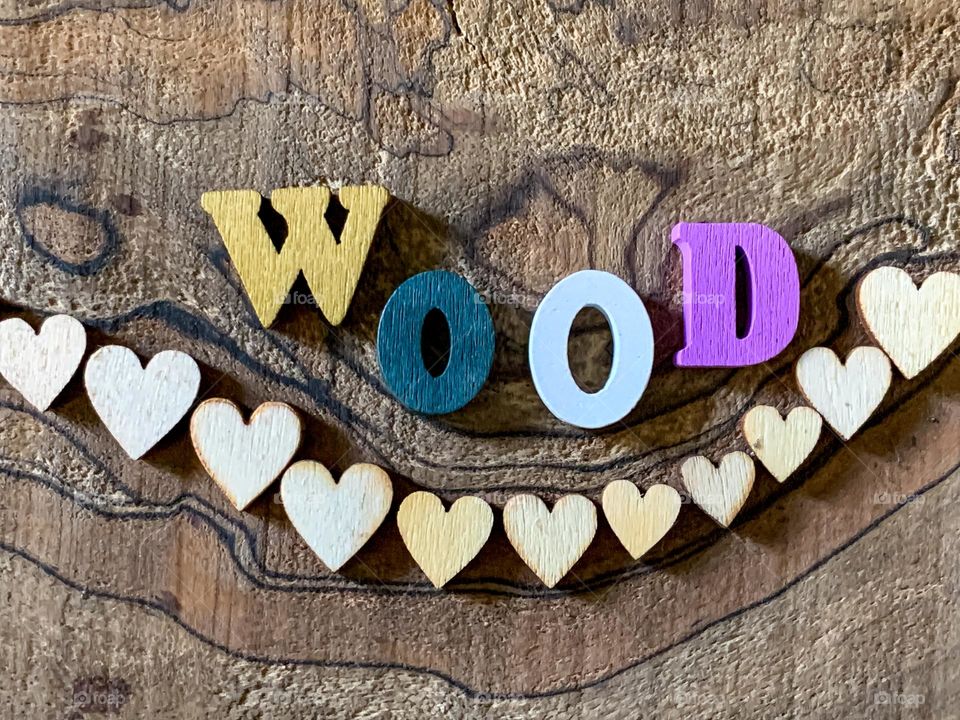 The word “wood” spelt out in coloured wooden letters above a row of wooden hearts against a wood background 