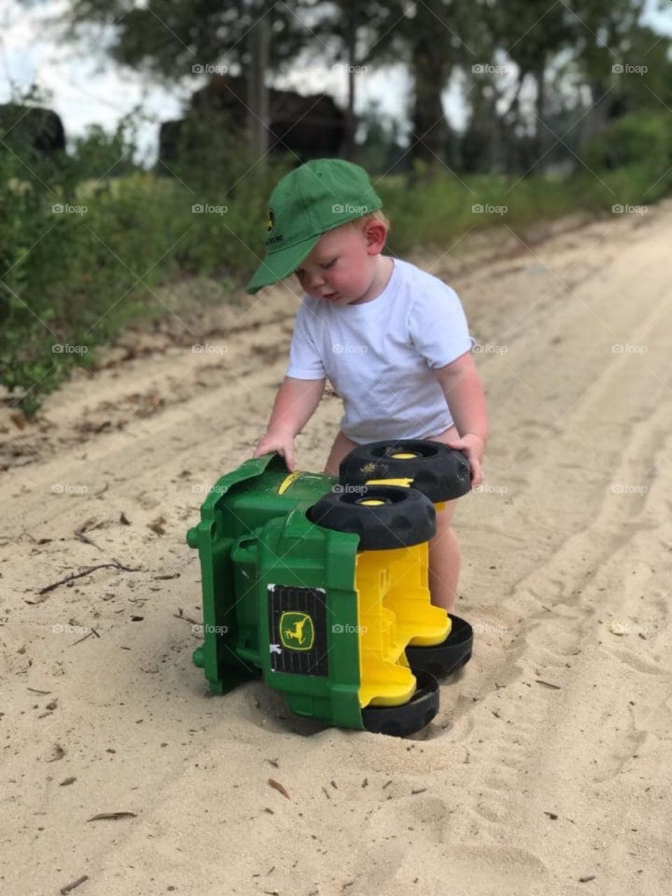 Toddler playing with john deer tractor wearing john deer hat