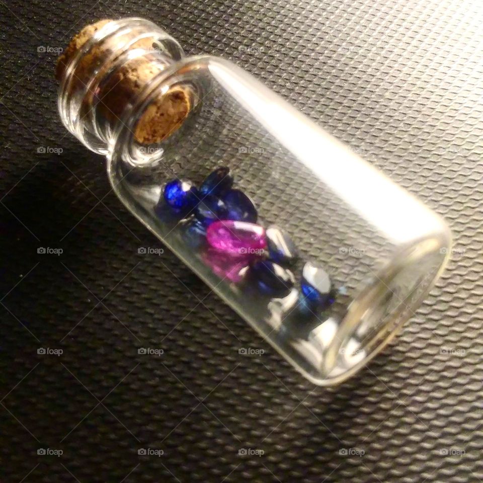 cobalt blue sapphires and pink Kashmir sapphire in a mini glass bottle on its side.