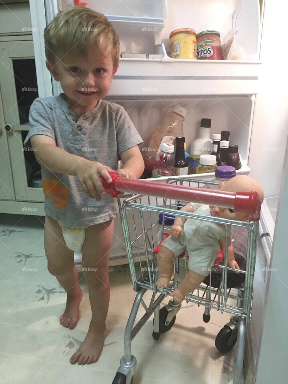 Little boy taking his baby shopping out of the refrigerator. 