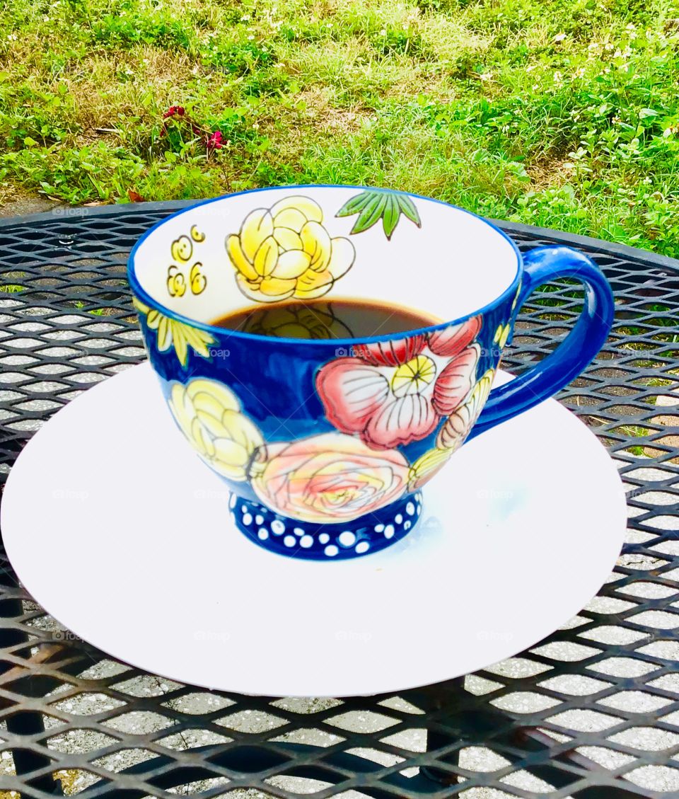 Cup of coffee! Beautiful dark blue floral cup on a ironing black table on the background green grass 