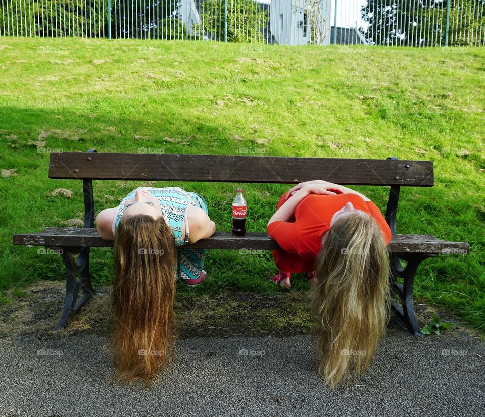 Sisters sharing a bottle of Coca-Cola larking about on a park bench ...