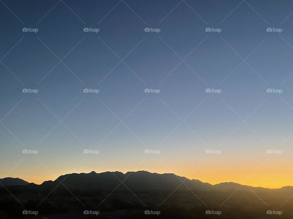 A yellow and orange sunset with mountains and the night sky above.