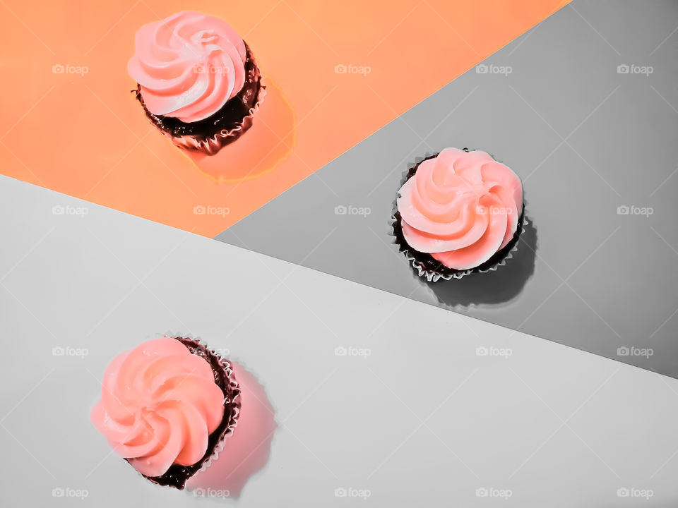 Flat lay of three peach colored frosting chocolate cupcakes divided each in a gray or peach triangular surface.