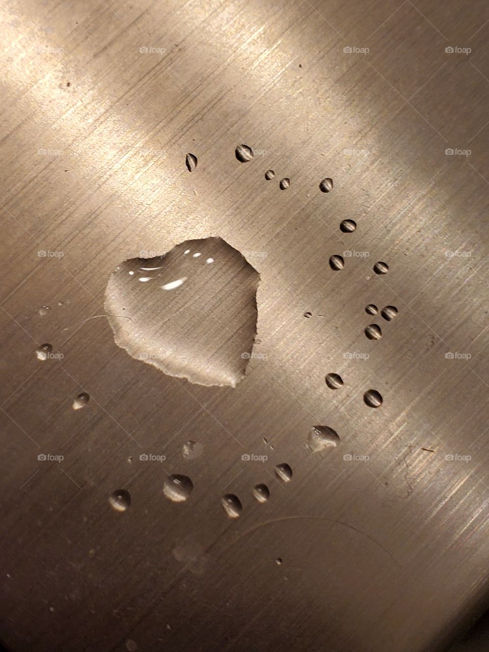 A heart shaped water droplet on a shiny stainless steel surface.