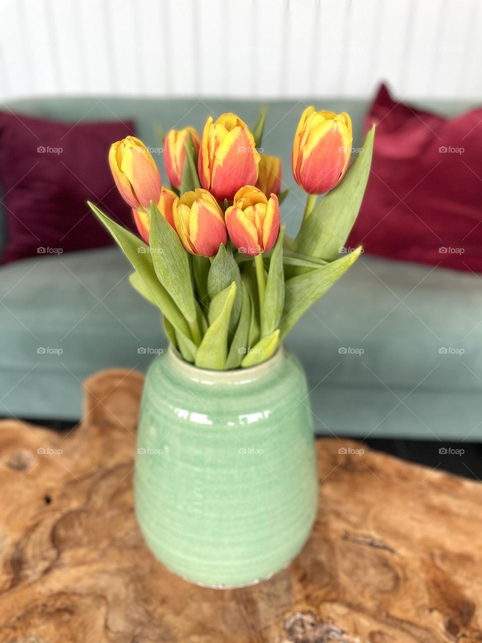 Beautiful red yellow tulip bouquet in a green ceramic vase on wooden table 