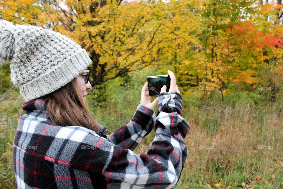 Young woman taking a photo of trees in the fall