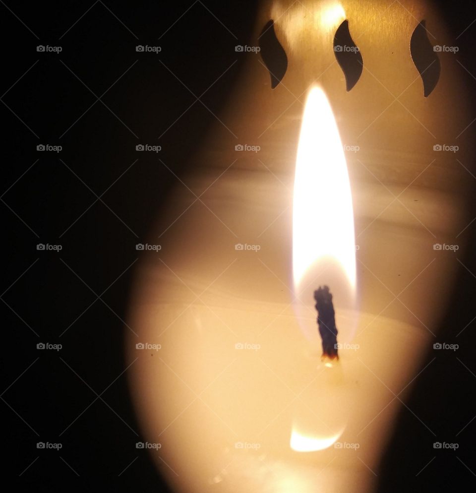 A macro view of a bright flame standing tall through the flame shaped holes of its container.