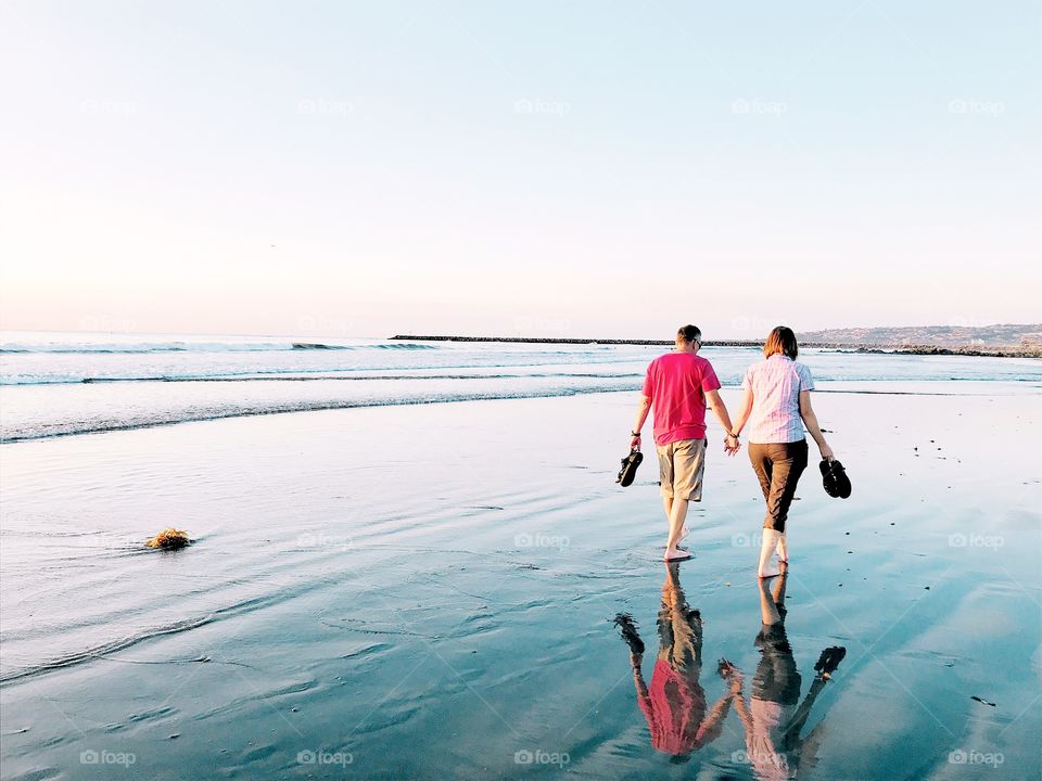Happy loving couple walking barefoot on the beach at low tide, holding hands. 