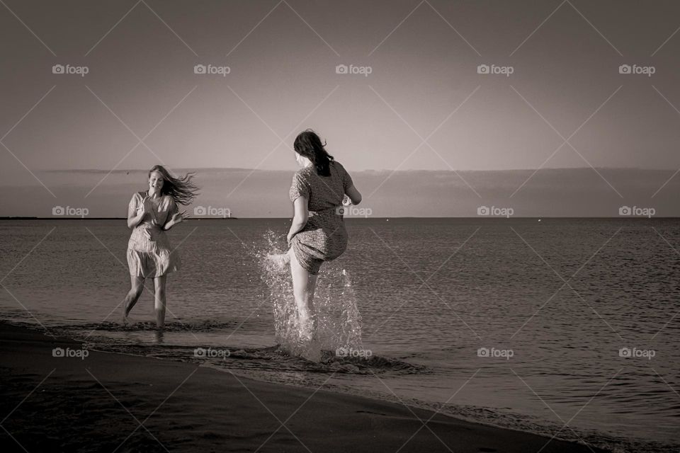 two female young sisters splashing in the sea on a summer night at sunset