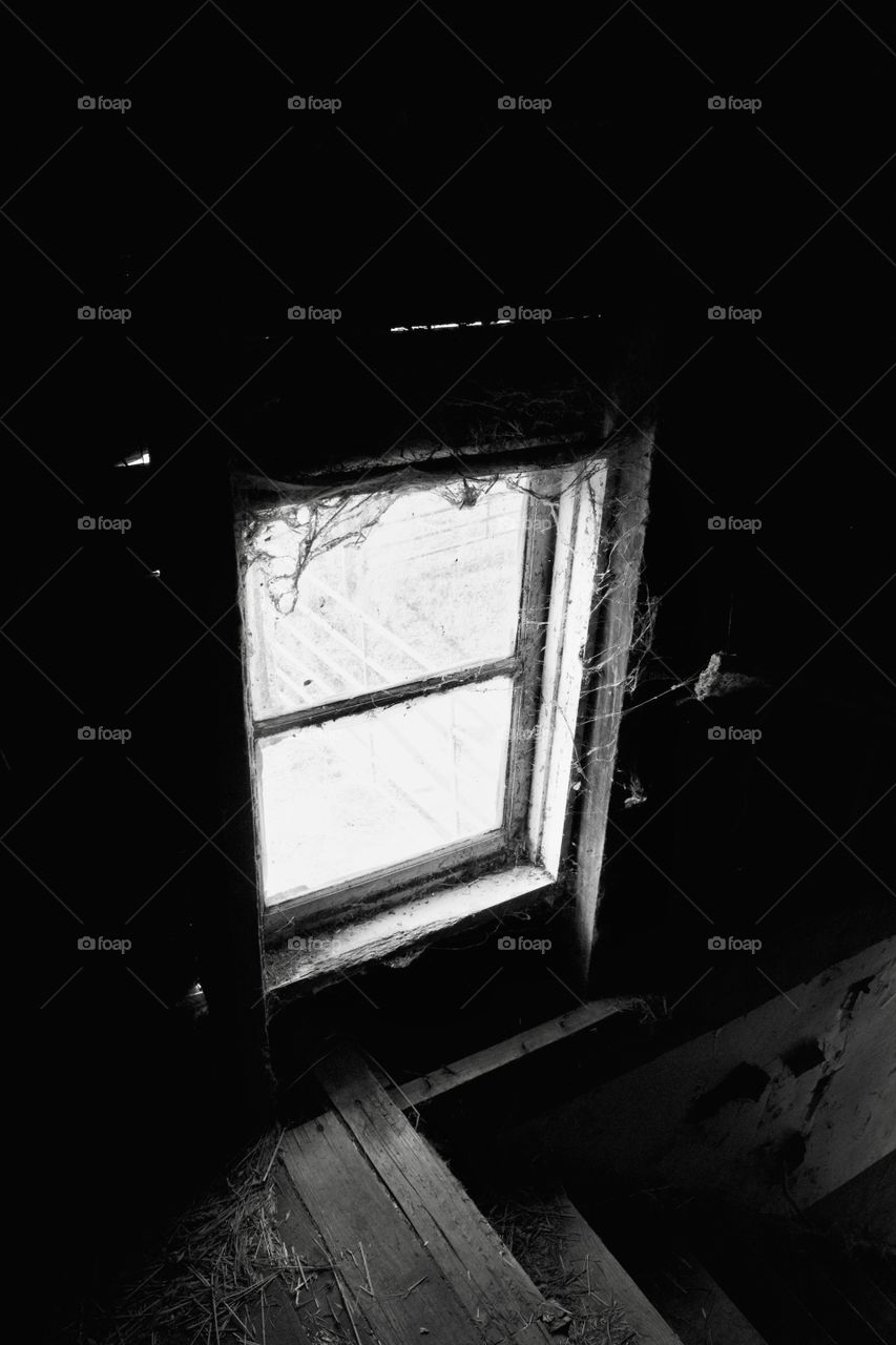 A cobweb-covered, hayloft window in an old, dusty barn in black-and-white