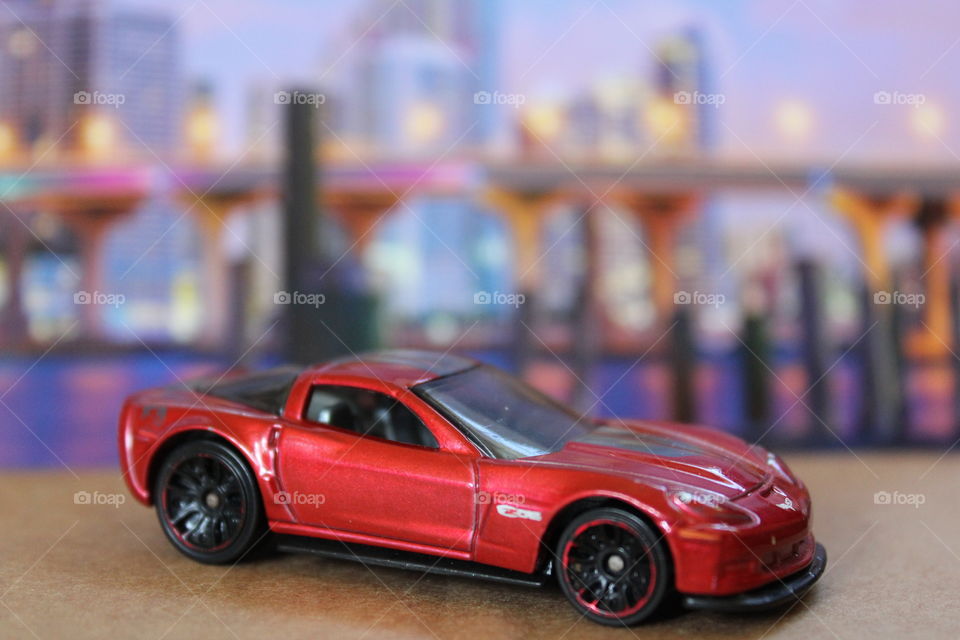 This is an up close picture of a red car with a city in the background.