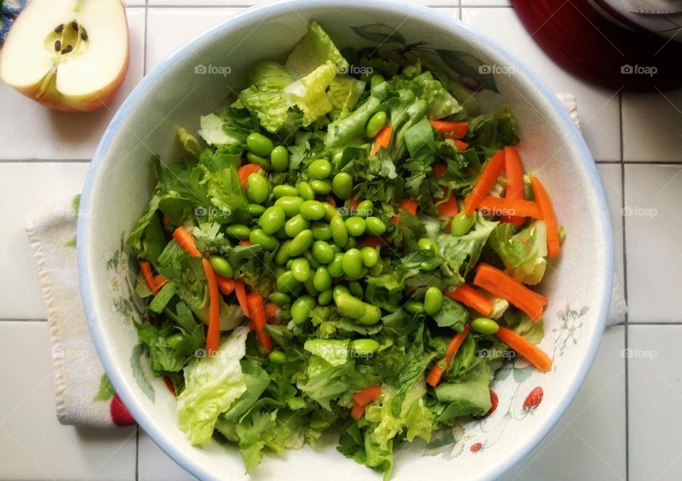 Stay fit by eating your greens, a salad with edamame romaine lettuce apple carrots & red bell pepper in a large bowl on a kitchen counter