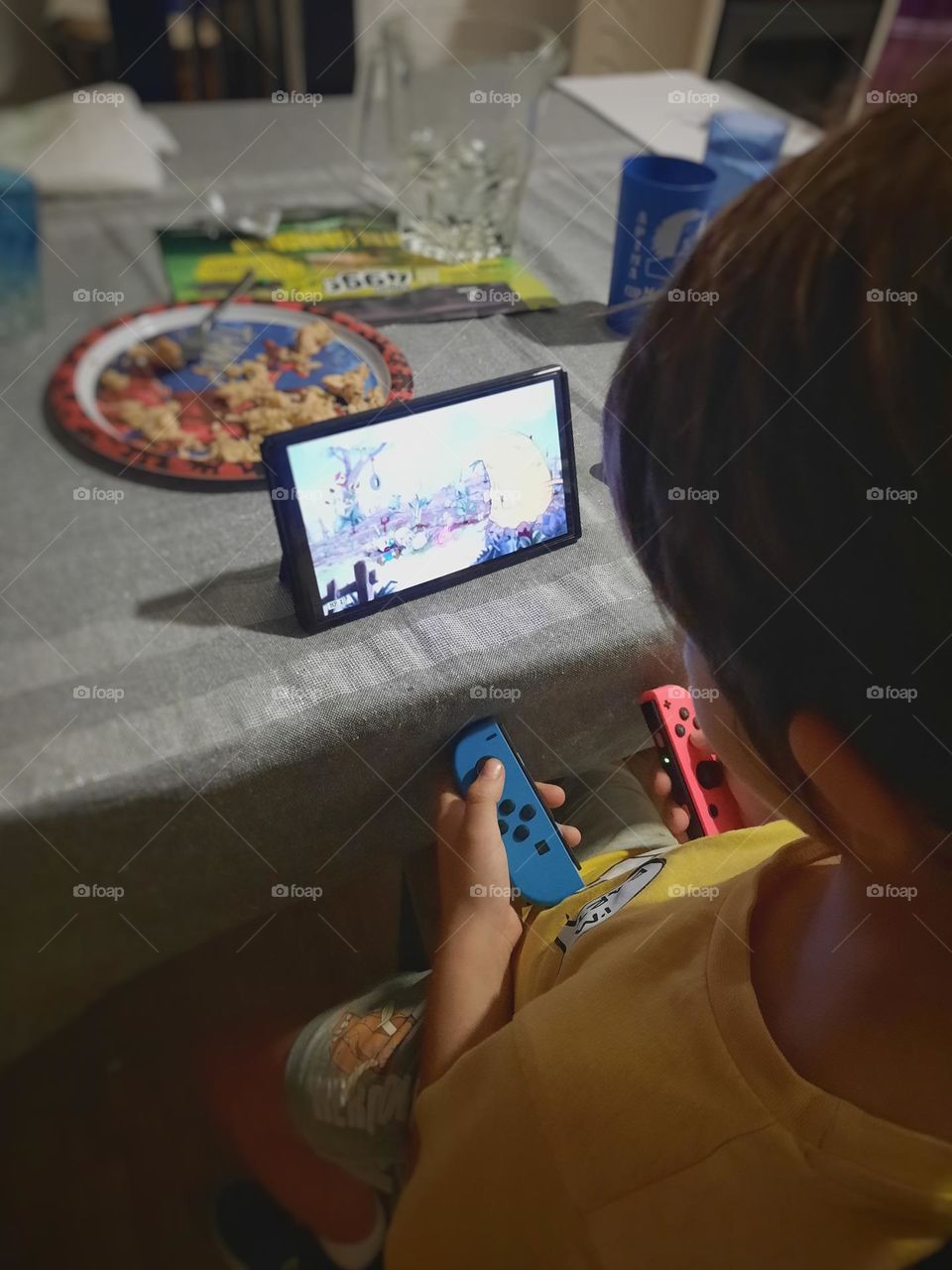 Child playing with his oled switch at the dining room table.