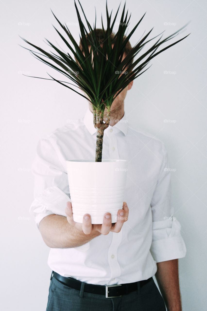 Portrait of a young man holding a plant in front of his head