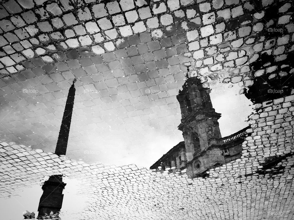 Piazza navona monuments reflected on a puddle of water in a cobblestone pavement