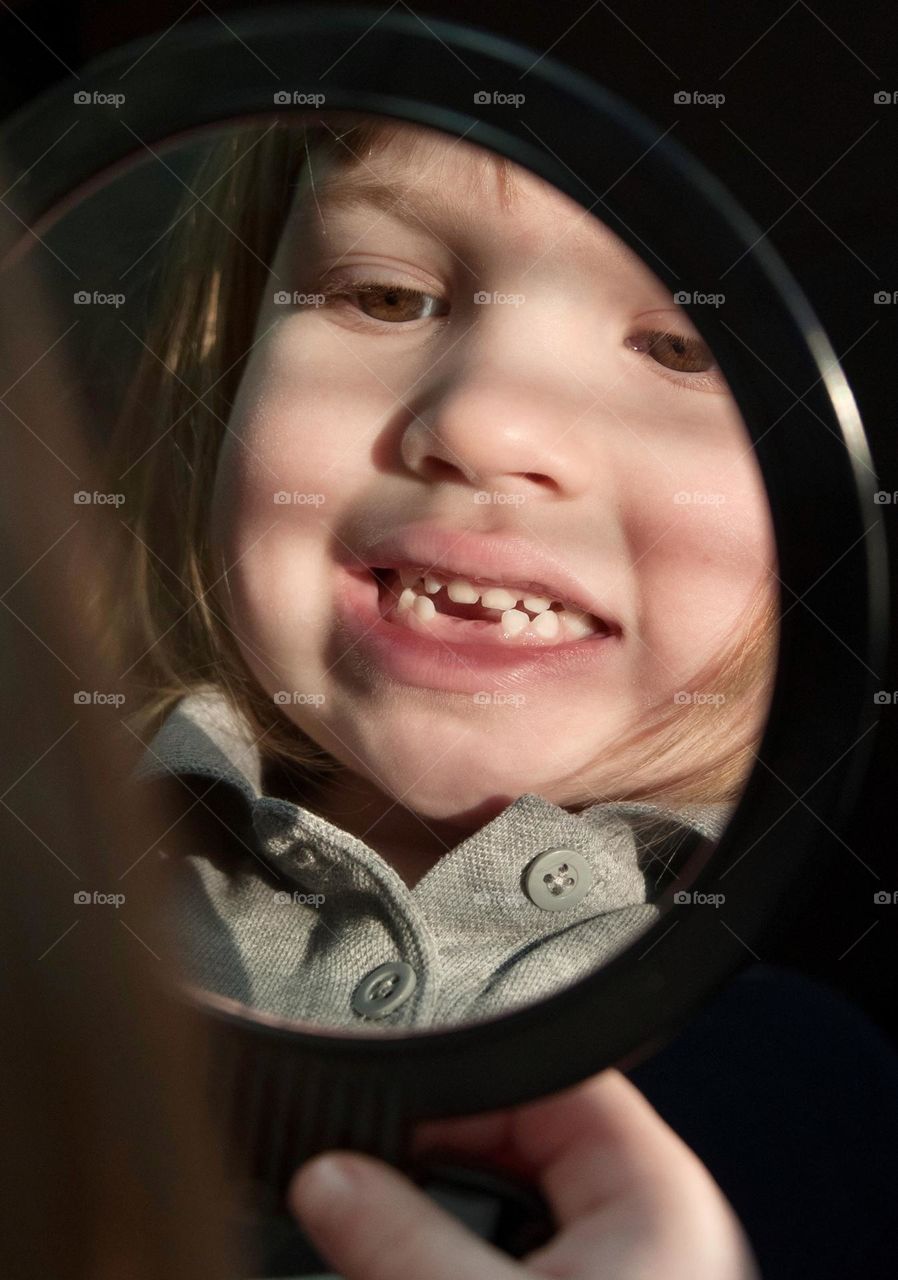 Little girl looking in the mirror at her missing teeth