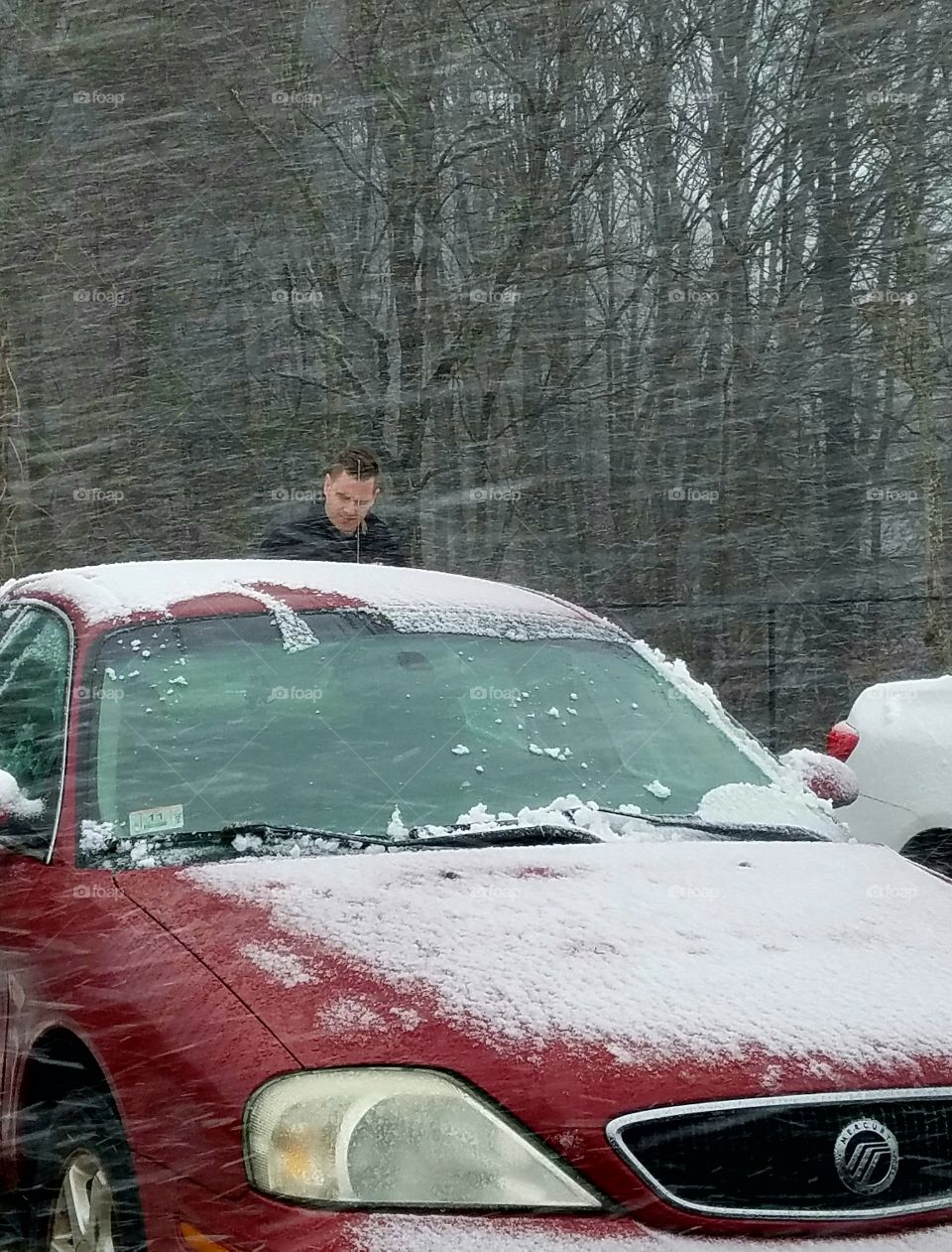 Wet snow blowing as person clears off car in parking lot.
