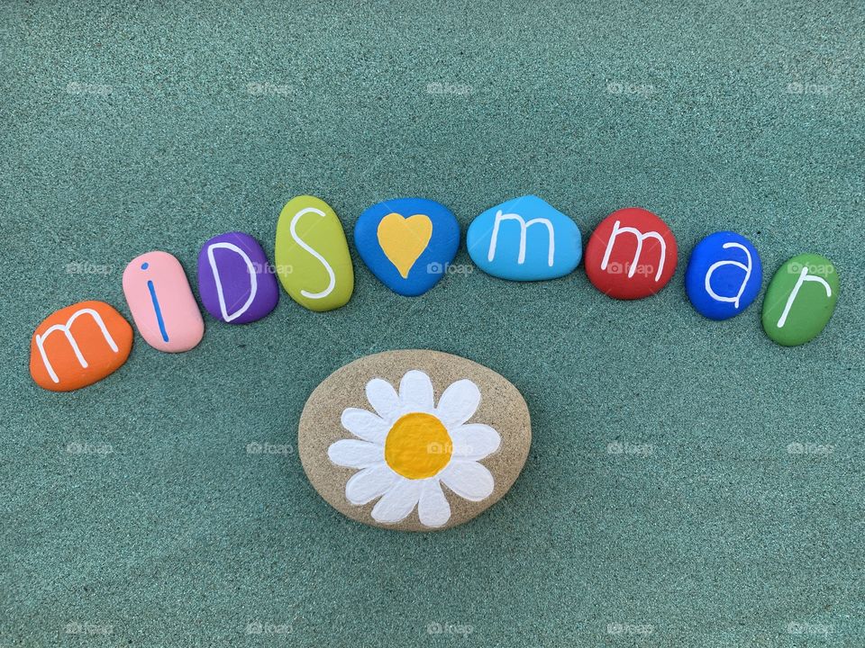 Midsommar festival celebrated with colored stones and a daisy painted on a stone over green sand