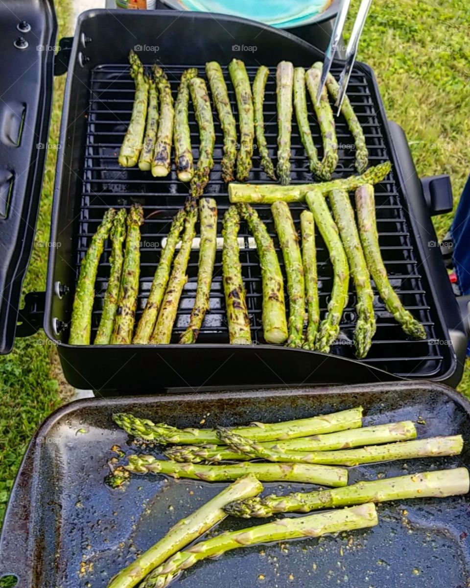 Rows of fresh asparagus laid out on a black grill at a summer cookout