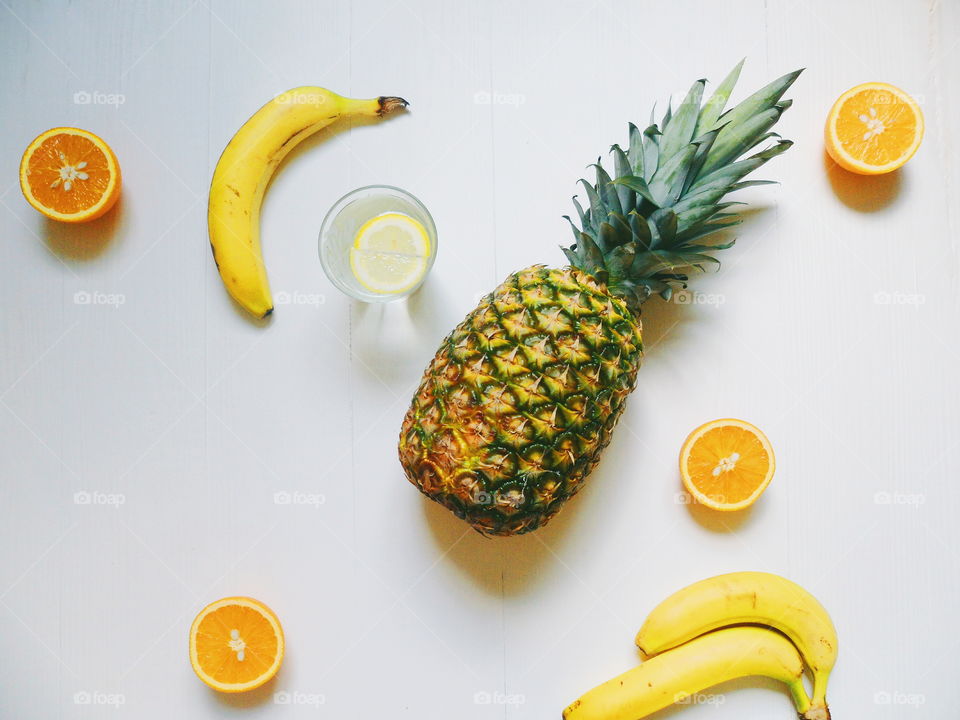 pineapple, bananas, sliced ​​oranges and a glass of lemonade on a white background