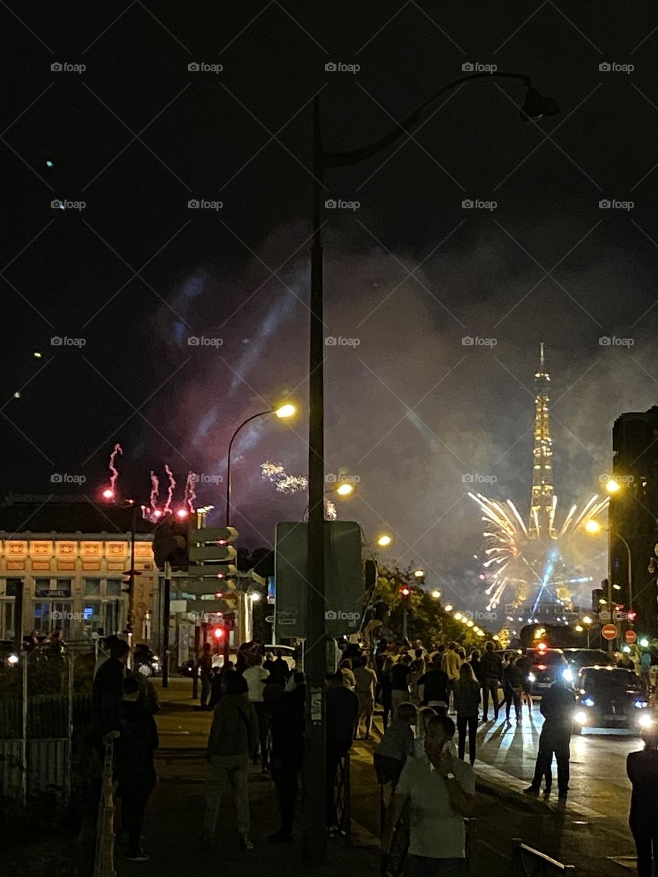 Night photo of Paris busy street with crowd watching Eiffel tower with fireworks.