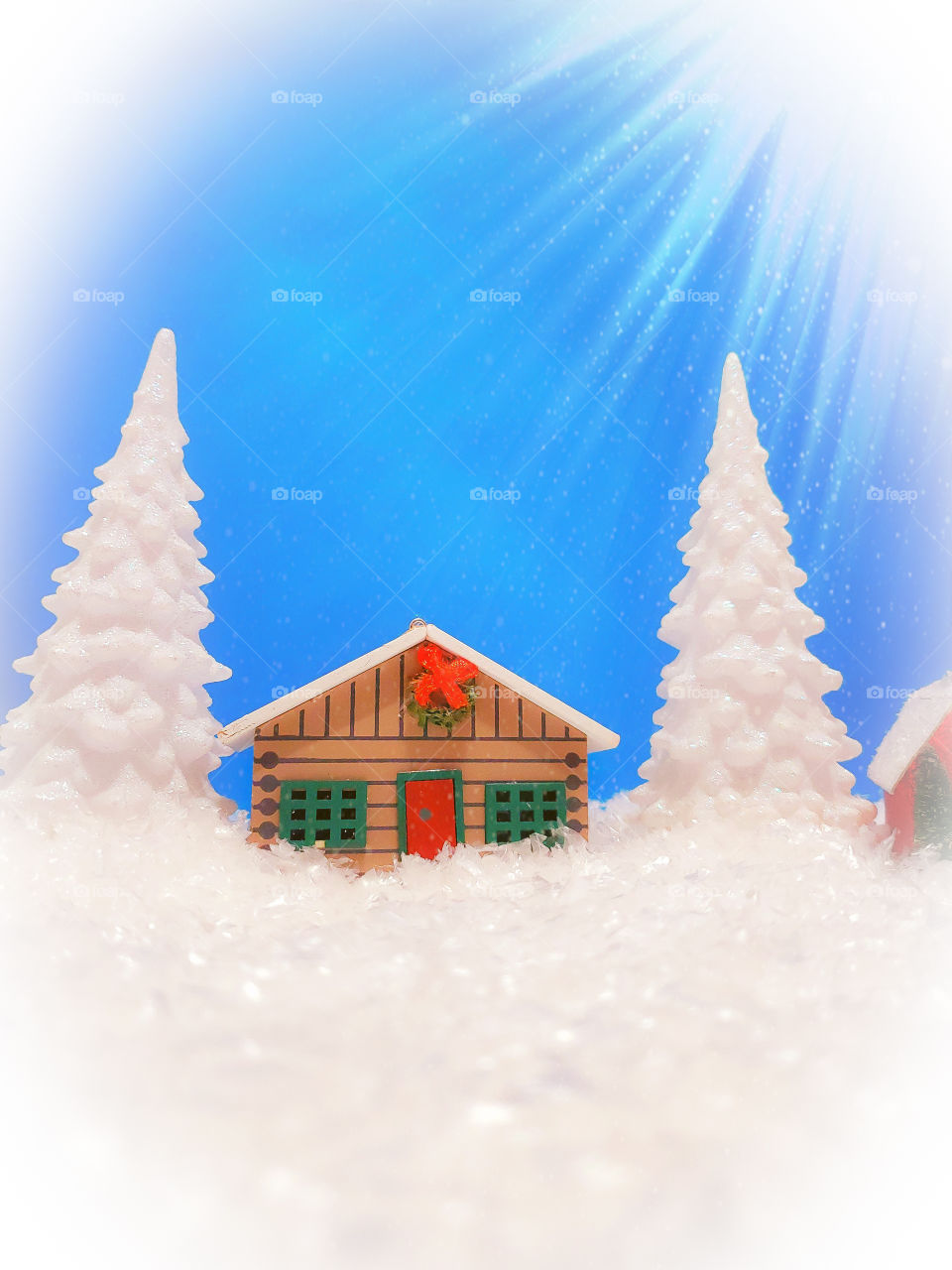 Winter miniature scene of a log cabin and two snow covered pine trees surrounded by snow with shining light from right corner.