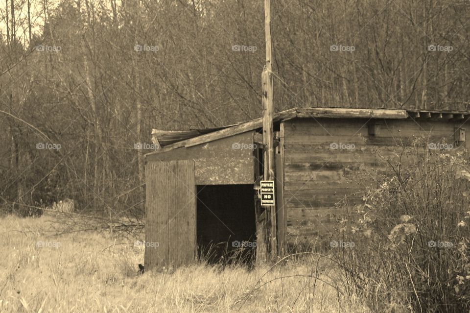 An old, unoccupied, doorless, dilapidated, wooden building with a No Trespassing sign in the middle of an open field. 
