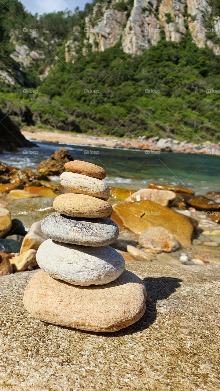 A stack of rounded pebbles stacked in one another, with the ocean and beach in the background.