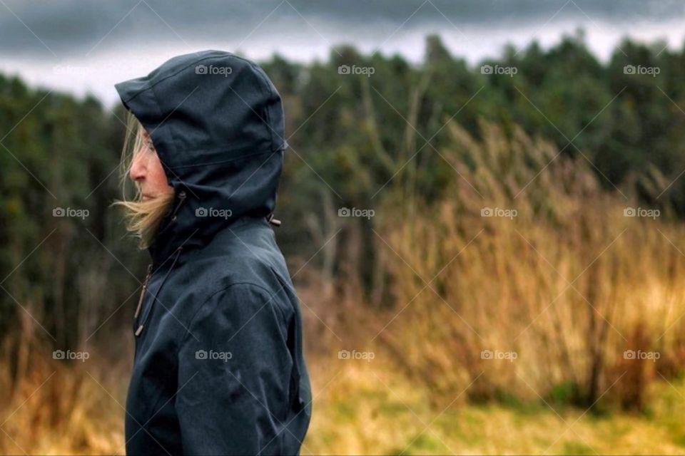 A woman in a raincoat stands in the forest in stormy autumn weather