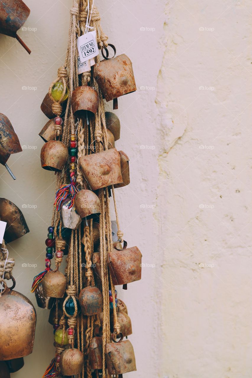 Small and bigger metal bells for sale are hanging out on the wall from a shop 