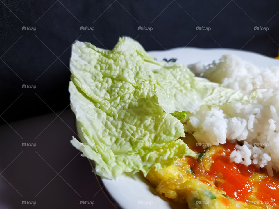 a plate of white rice accompanied by a side dish of fried eggs and fresh vegetables